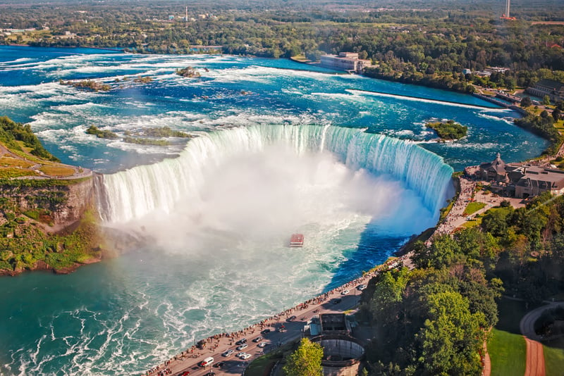 Aerial top landscape view of Niagara Falls and tour boat in water between US and Canada.  Horseshoe of famous Canadian waterfall on sunny day